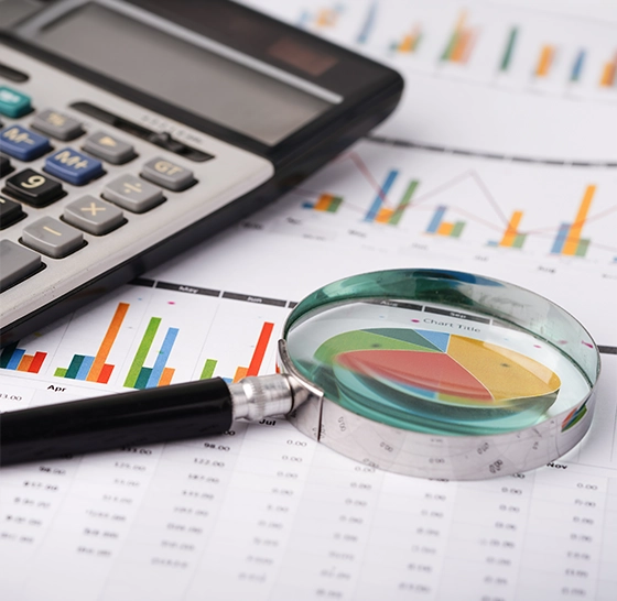 Close-up of a magnifying glass highlighting a pie chart next to a calculator, representing detailed data analysis in ethnography.