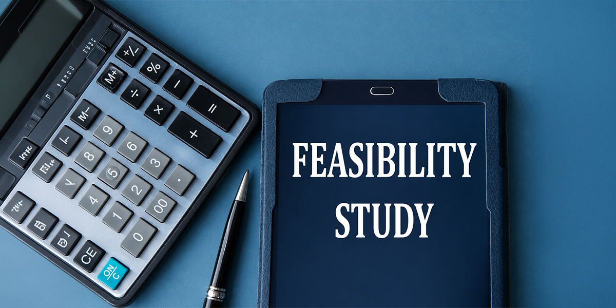 Company Feasibility Study concept with a calculator, pen, and tablet displaying “FEASIBILITY STUDY” on a blue background.
